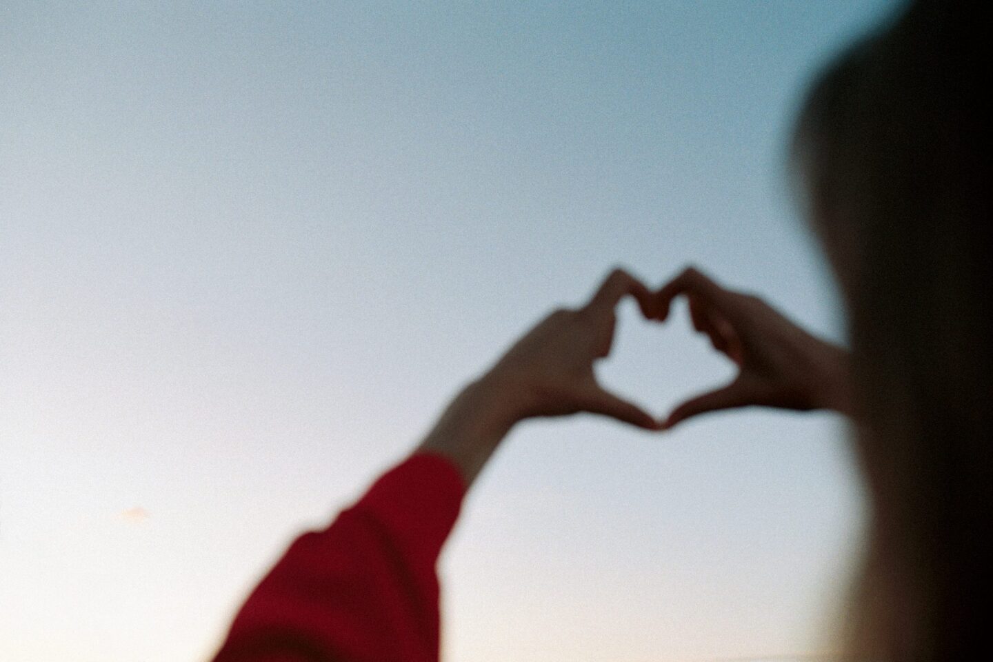 Person formar händerna som ett hjärta mot himlen.