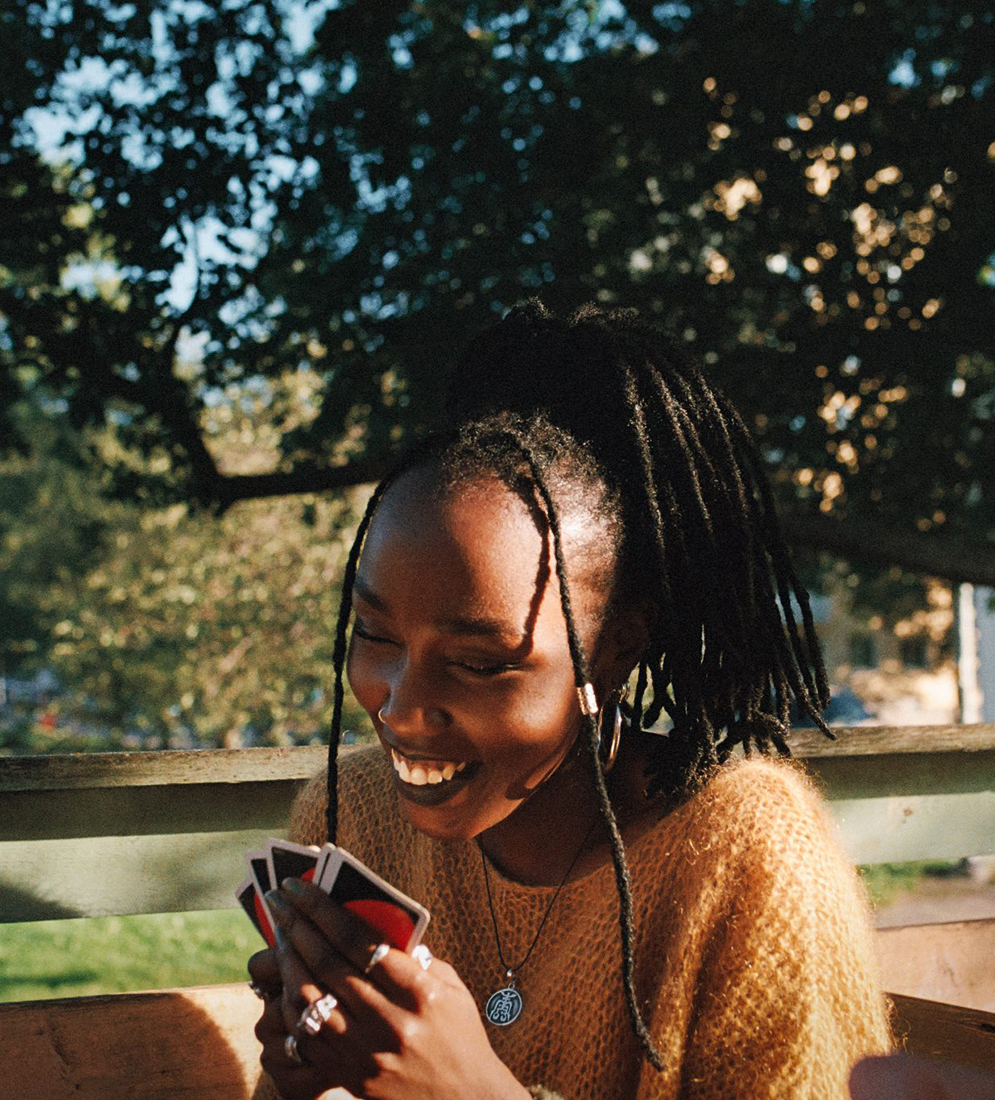 Kvinna sitter utomhus i solsken. Hon ler och tittar in i en smartphone.