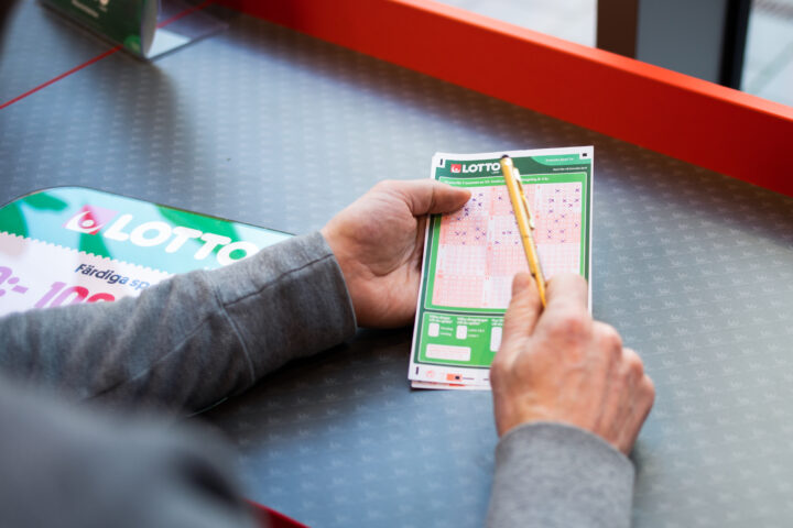 Händer som håller en Lotto-kupong vid en spelbutiks kassa.