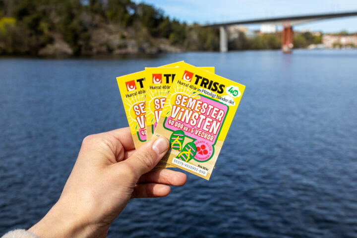 Hand håller tre Triss Semestervinsten-lotter framför vatten och en bro i bakgrunden.